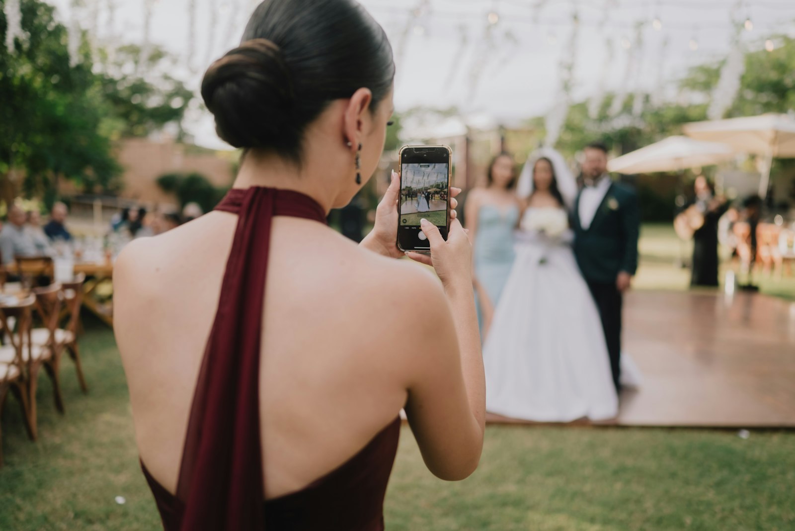 Hochzeitsgast im weinroten Kleid fotografiert das Brautpaar mit dem Smartphone