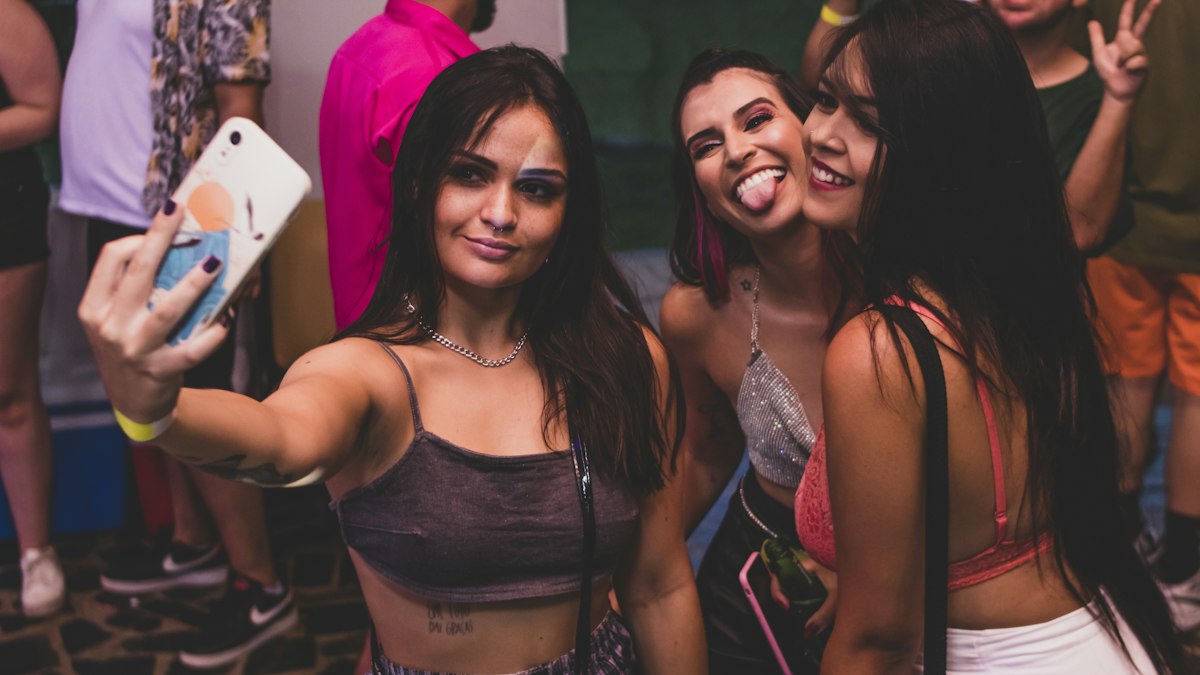 Zwei Frauen machen ein Selfie, hinter ihnen feiert eine Gruppe