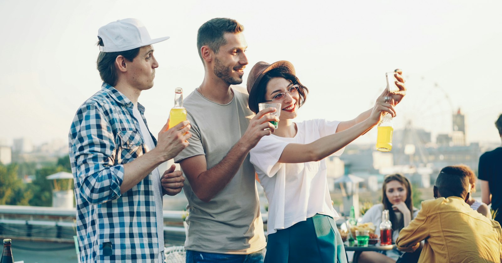 Freunde machen auf einer Dachterrassen-Party lachend ein Selfie mit dem Handy