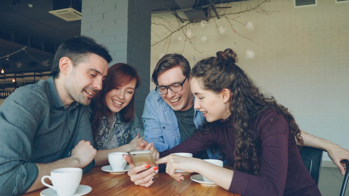 Freunde schauen gemeinsam auf ein Handy und lachen über Fotos