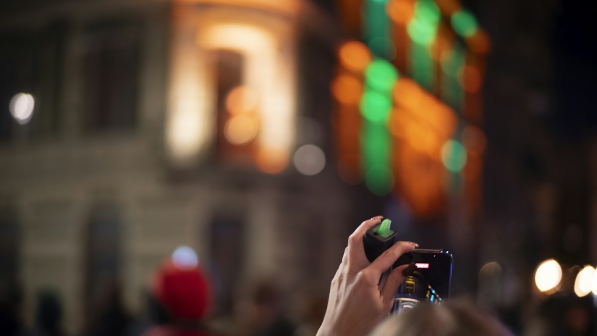 Hand hält ein Smartphone bei einer Abendveranstaltung mit bunten Lichtern